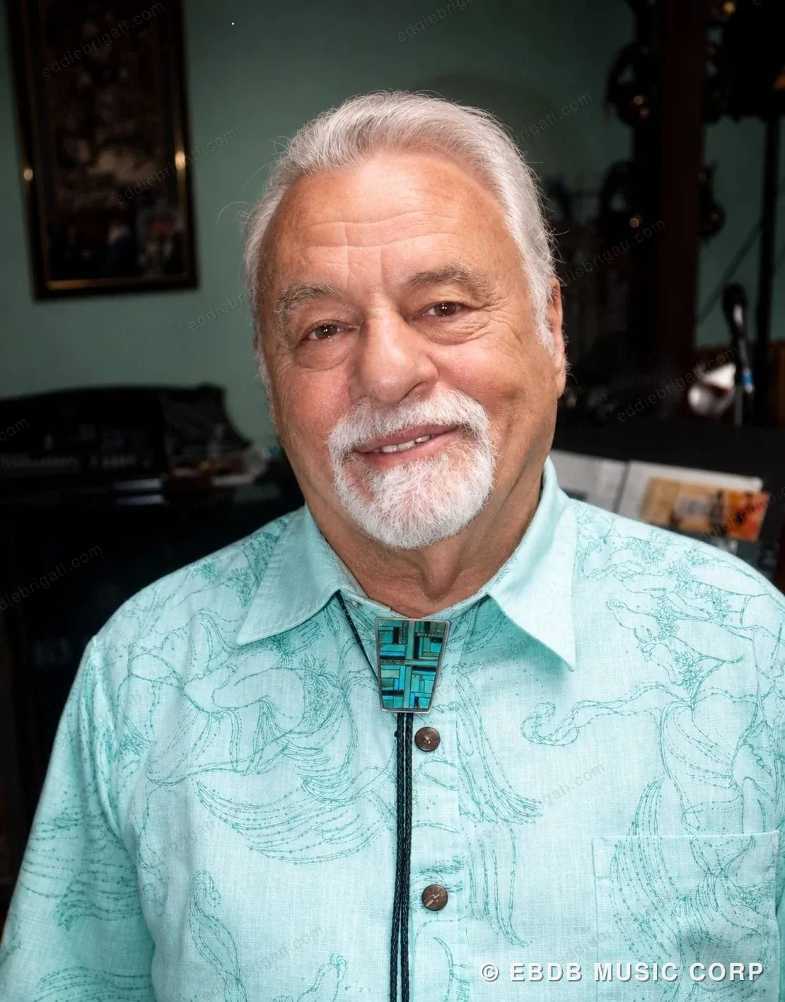 A recent color portrait of Eddie Brigati — grey hair, white beard, wearing a teal patterned shirt with a bolo tie.