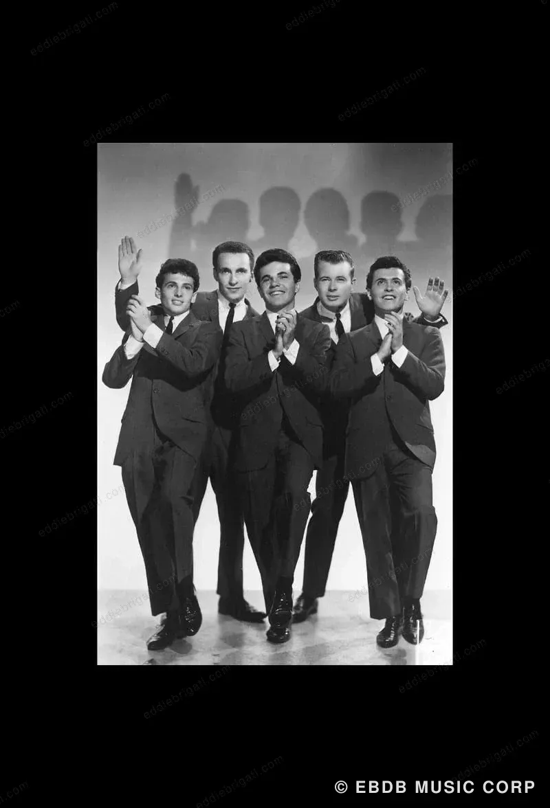 A black-and-white publicity photograph of five young men in matching suit jackets and bow ties, mid-performance with hands raised, applauding.