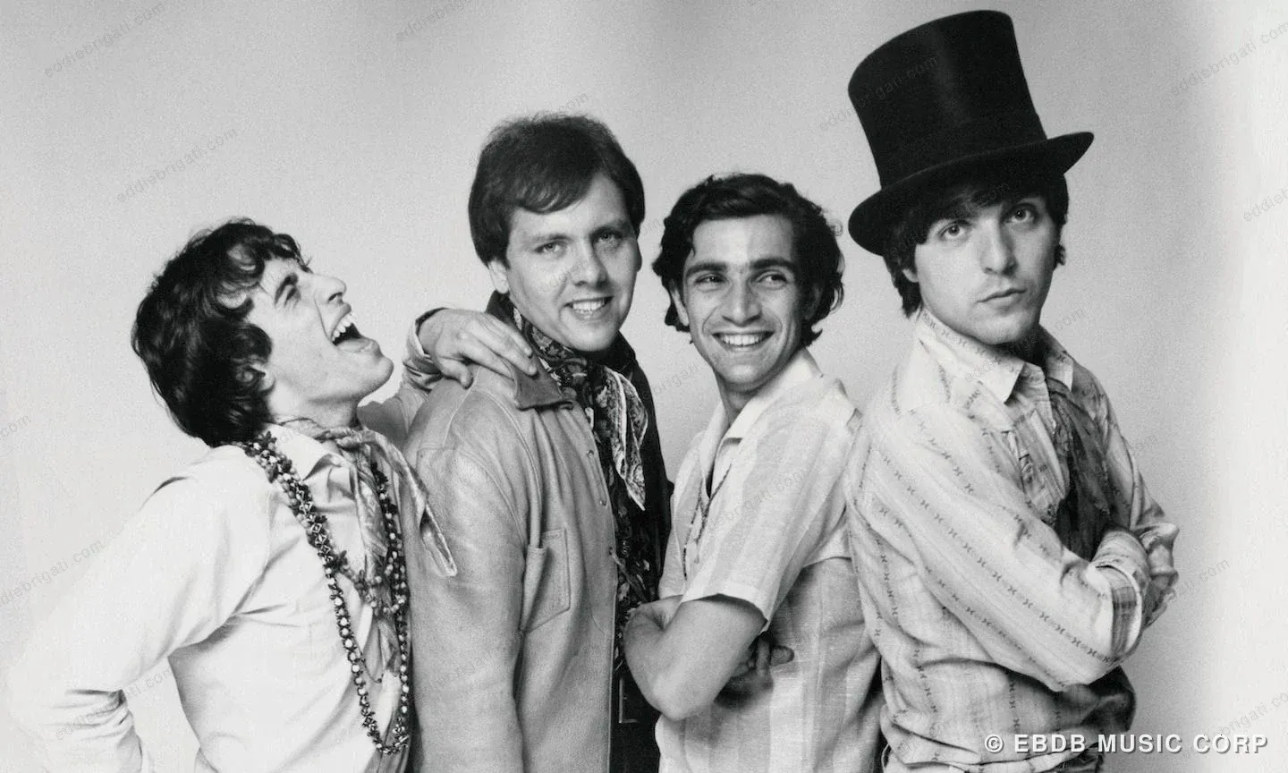 A black-and-white publicity photograph of four young men, one wearing a top hat, posed together with arms crossed.